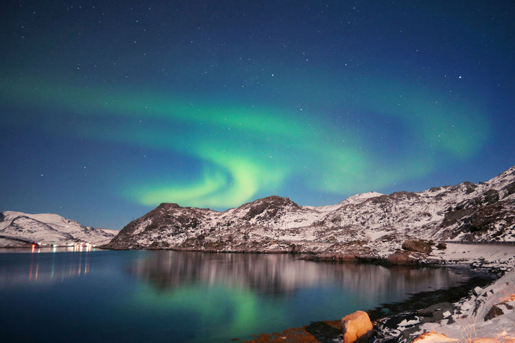 Stunning dancing northern lights over snowy mountains and sea coast in lofoten islands, norway. 