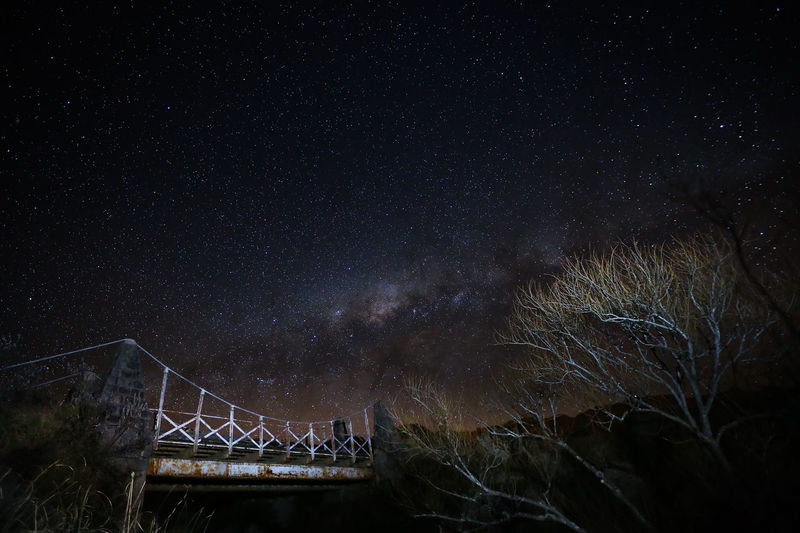 Low angle view of old bridge by bare trees against milky way