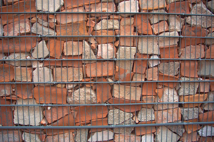 A loose brick wall kept in place by a metal fence 