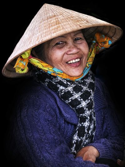 Portrait of smiling woman wearing asian style conical hat against black background