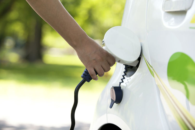 Cropped hand of person charging white electric car