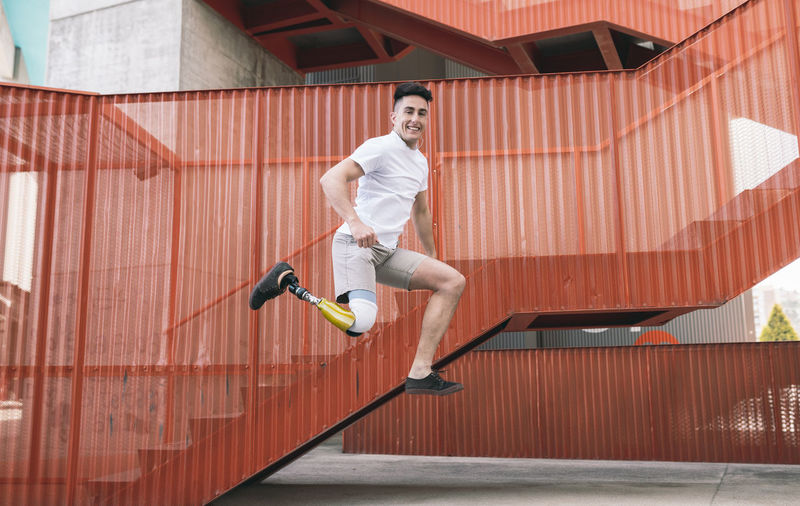 Young disabled man jumping against orange staircase