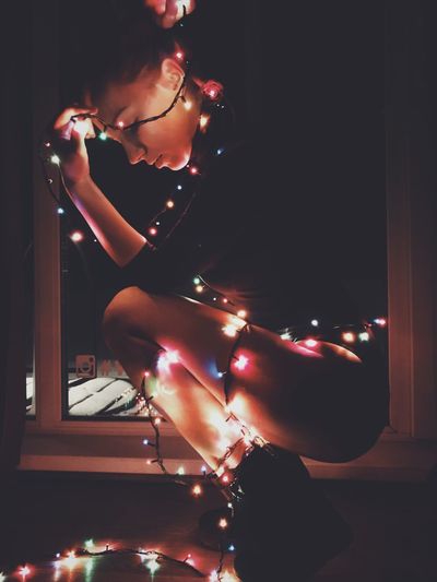 Side view of woman with illuminated string lights crouching in darkroom