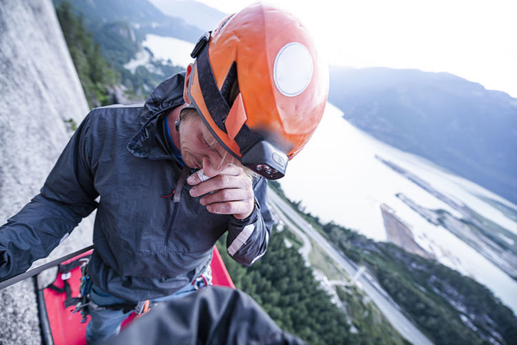 Climber with helmet scratching his nose standing on portaledge sunset