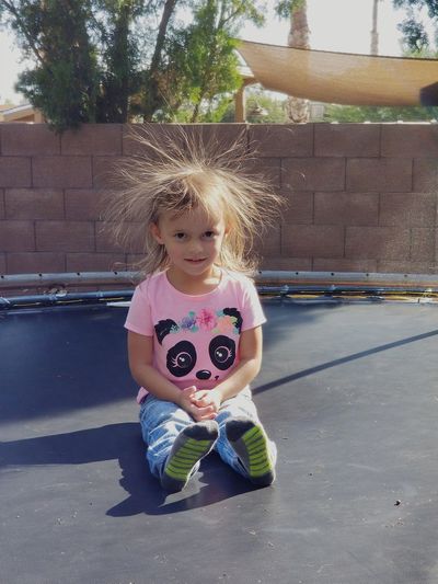 Portrait of cute girl with hair standing on end sitting on trampoline