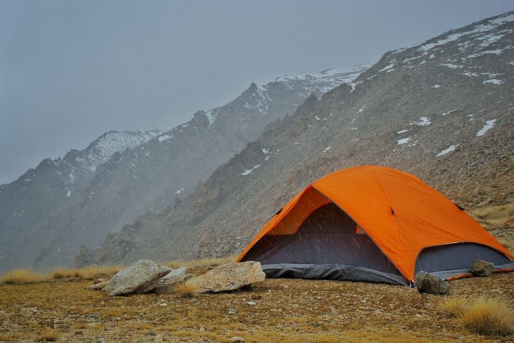 Orange color tent being set up by trekkers  in the mountains in ladakh and a space for text