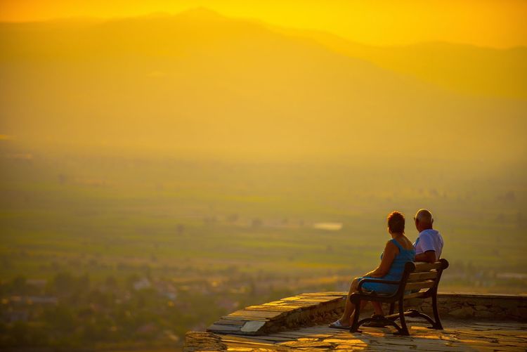 View of couple sitting on landscape against sky during sunset