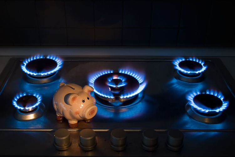 High angle view of piggy bank by illuminated burners in kitchen at home