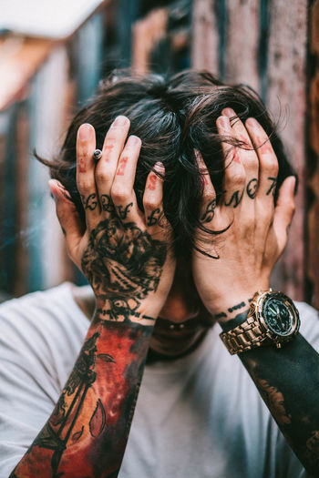 Close-up of depressed tattooed man sitting with head in hands outdoors