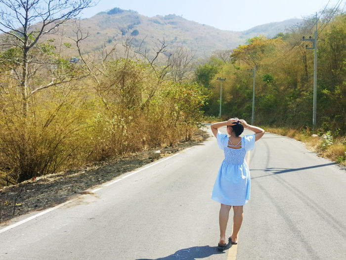 Rear view of woman walking on road during sunny day