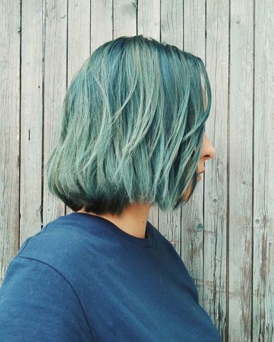 Side view of woman with green dyed hair by wood paneling