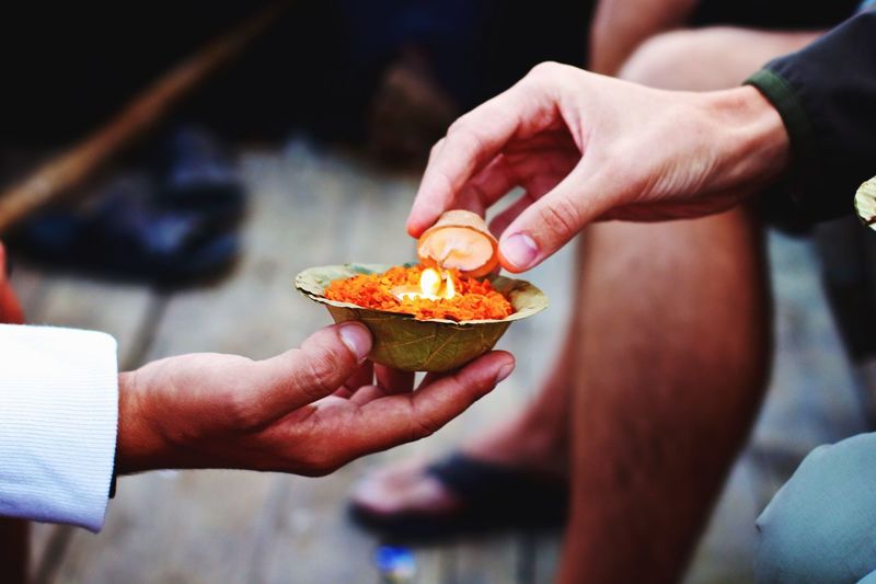 Midsection of men holding lit diyas with religious offering in container