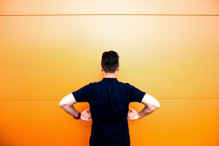 Rear view of man standing against orange wall