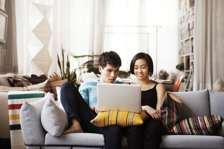 Young couple using laptop while sitting on sofa at home