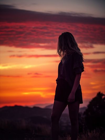 Woman standing against orange sunset sky