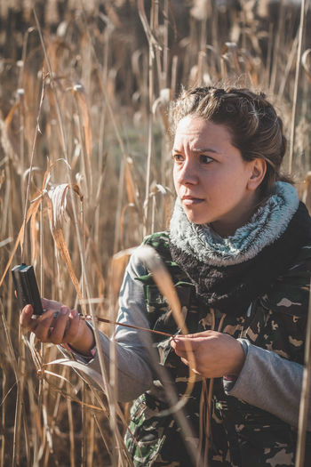 Woman holding mirror compass standing amidst field in forest
