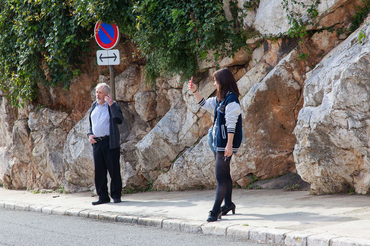 Woman with mobile phone standing on sidewalk by rock formations