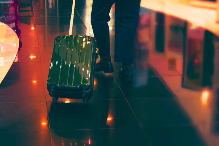 Low section of man with wheeled luggage on tiled floor