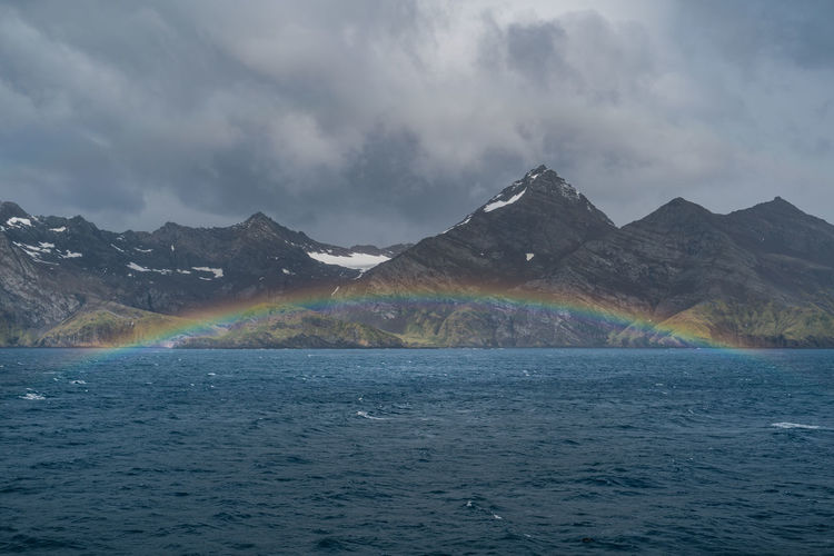 Scenic view of rainbow over sea and mountains against sky