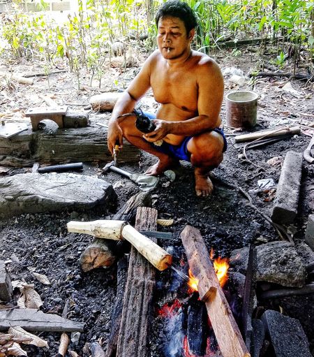 Full length of shirtless man sitting on wood