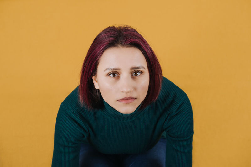 Portrait of young woman sitting against yellow background