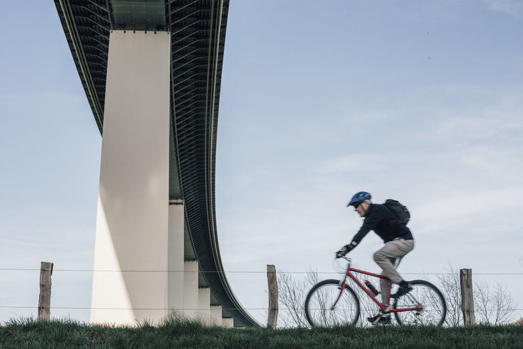Senior man riding bike, under bridge