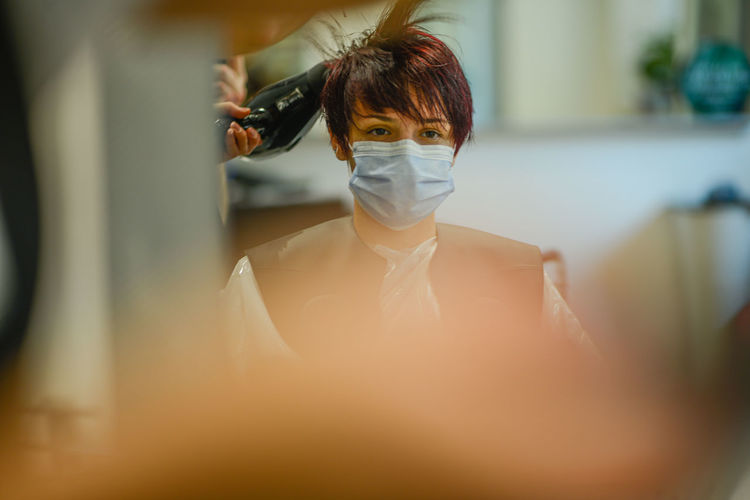 Female hair stylist at work wearing face mask while styling woman