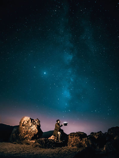 People sitting on rock against star field at night