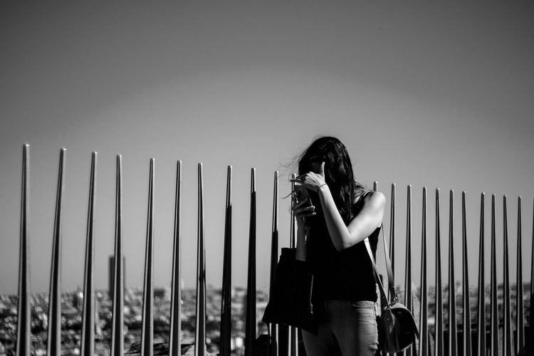 Woman using phone while standing by railing at arc de triomphe against sky