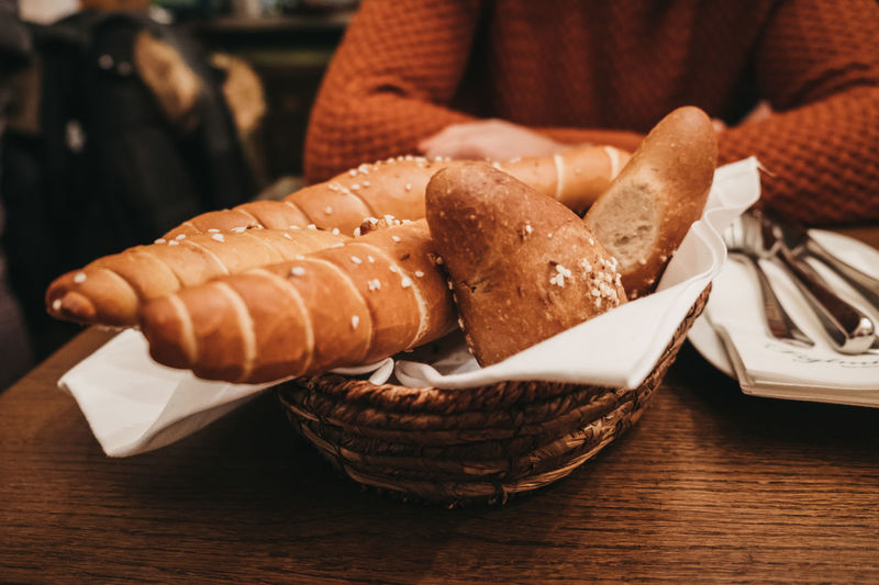Midsection of woman sitting by breads in wicker basket on table