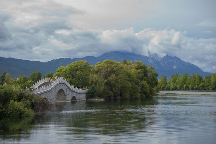 Arch bridge over river by mountains against sky