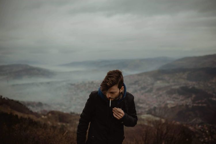 Man smoking cigarette while standing on mountain against sky