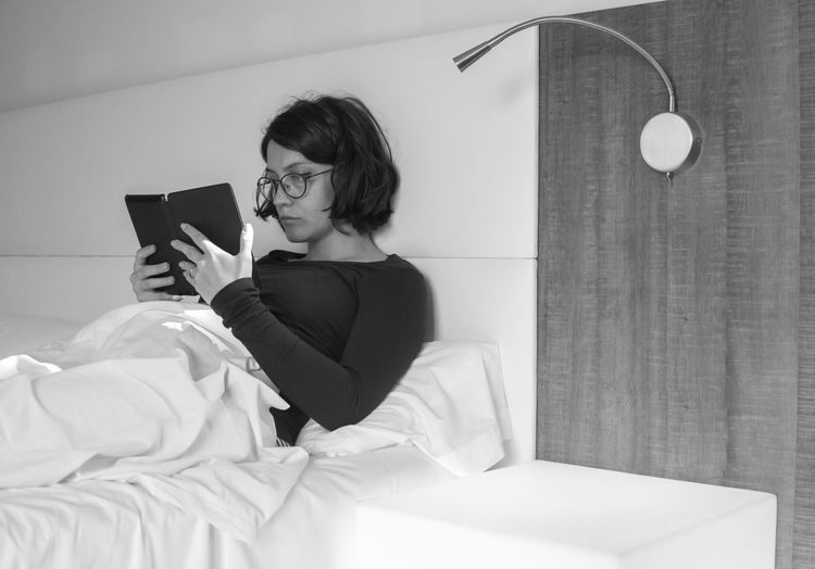 Young woman reading book on bed at home
