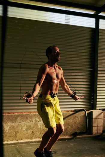 Full length of shirtless man standing against wall