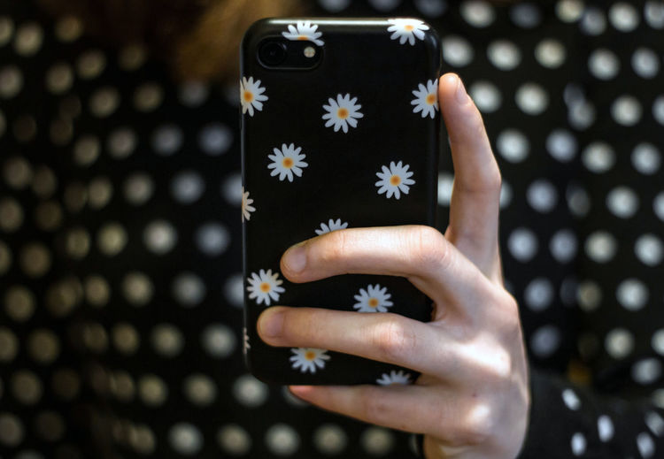 A young woman in a fashionable dotted jumper holds up her mobile phone, which is in a matching case