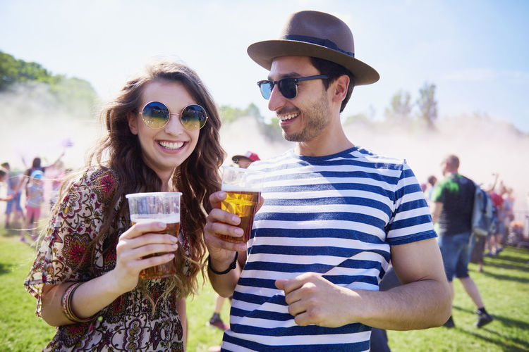 Man and woman with drinks standing on grass during music festival