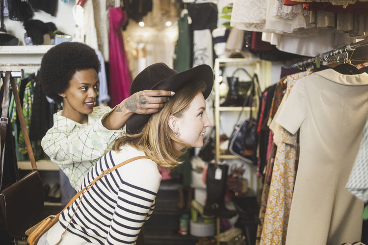 Store owner trying hat on female customer in boutique