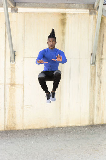 Young man doing jumping exercise on footpath in front of wall