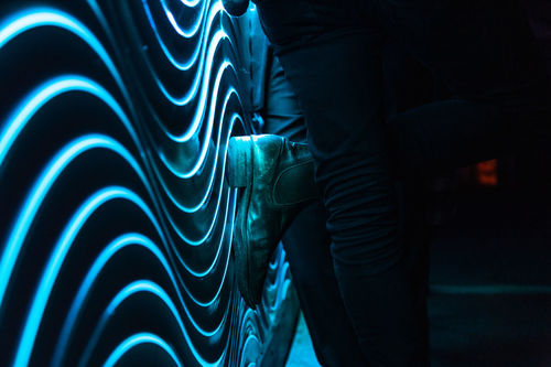 MIDSECTION OF MAN STANDING BY ILLUMINATED WALL AT NIGHT