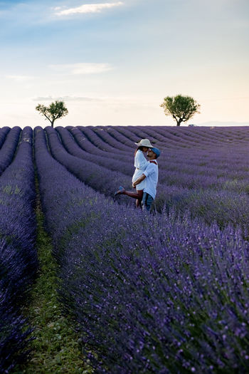 Rear view of couple standing on flowering field against sky