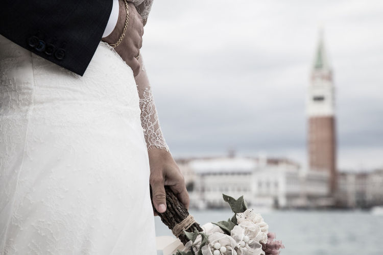 Cropped hand of bridegroom touching bride stomach against canal