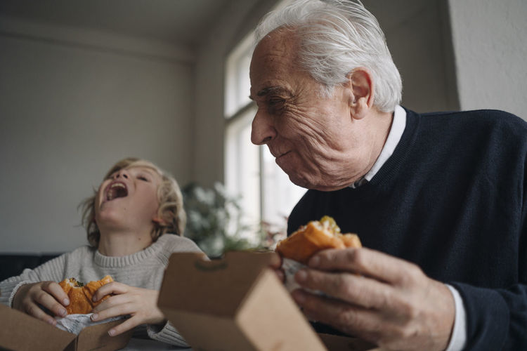 Happy grandfather and grandson eating burger together at home