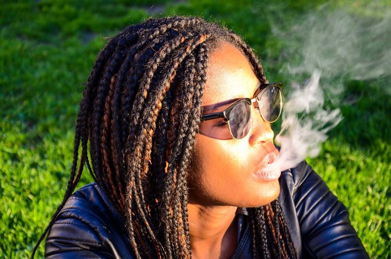 Close-up of young woman exhaling smoke on field