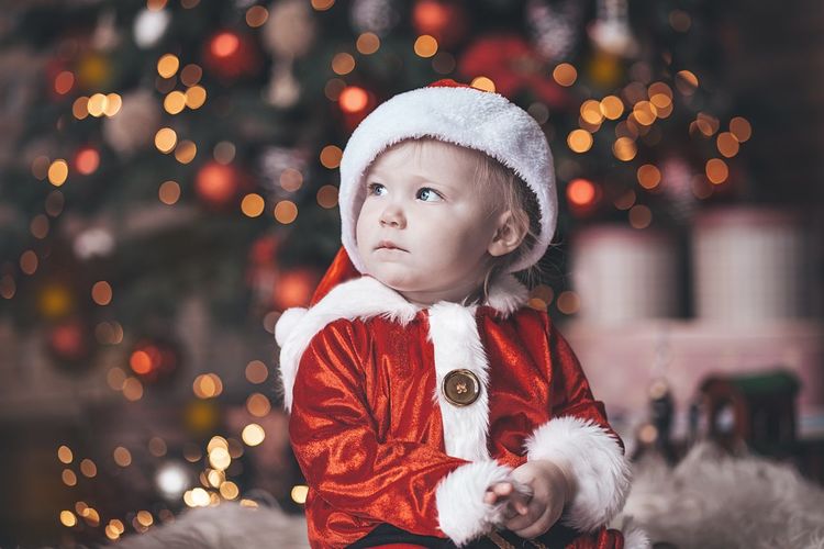 Cute girl in santa claus costume looking away against illuminated christmas tree