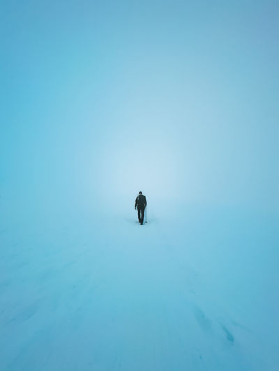 View of woman walking up the hill landscape cover in snow in a foggy winter conditions.