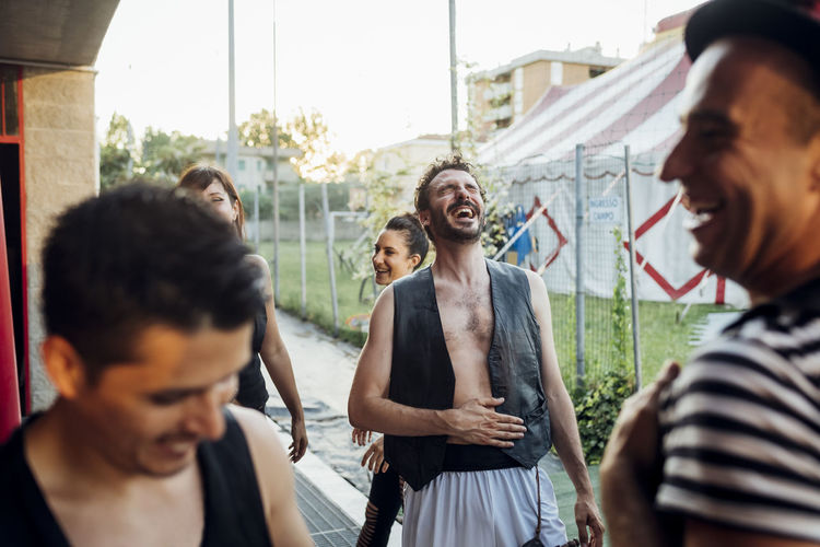 Male artist laughing while standing with acrobats on footpath