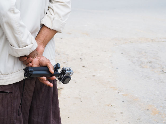 Midsection of man holding camera at beach