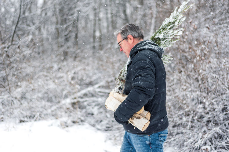 Side view of man carrying firewood during winter