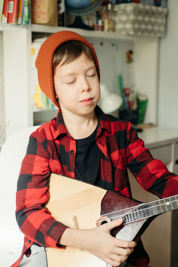 Boy in a red hat and a plaid shirt plays the balalaika. handsome boy holding his guitar.