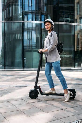 Young happy woman in casuals driving electric push scooter. businesswoman in cycling helmet 